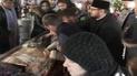 Верующие и священник заставляют женщину прикасаться к стеклу над мощами святой