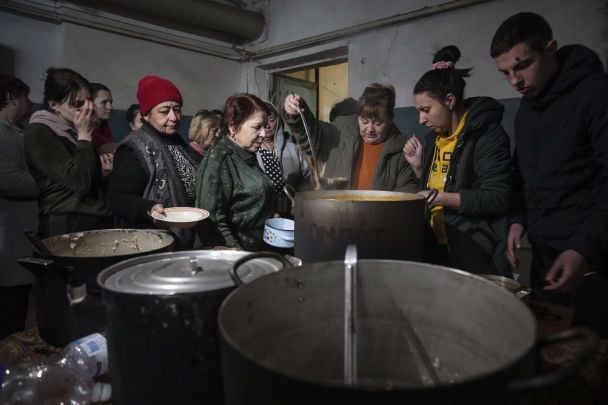 People queue to receive hot food in an improvised bomb shelter / © Associated Press