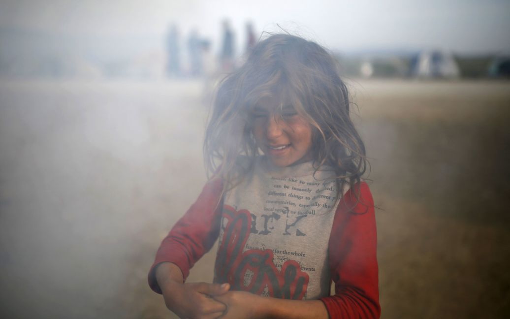 Дівчинка стоїть у диму в імпровізованому таборі для мігрантів та біженців на греко-македонському кордоні поблизу села Ідоменей, Греція. / © 