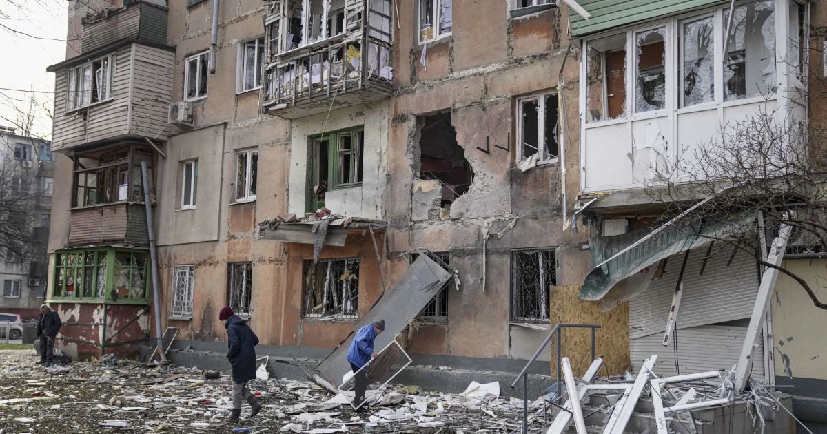 People walk next to an apartment building hit by shelling.