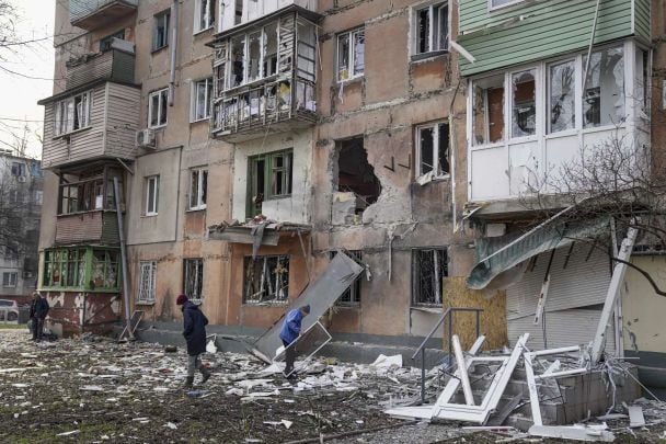 People walk next to an apartment building hit by shelling. / © Associated Press