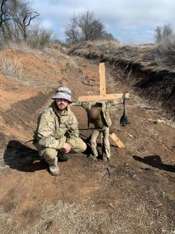 Владислав Пастух на фоне привязанного к кресту военнослужащего / © 