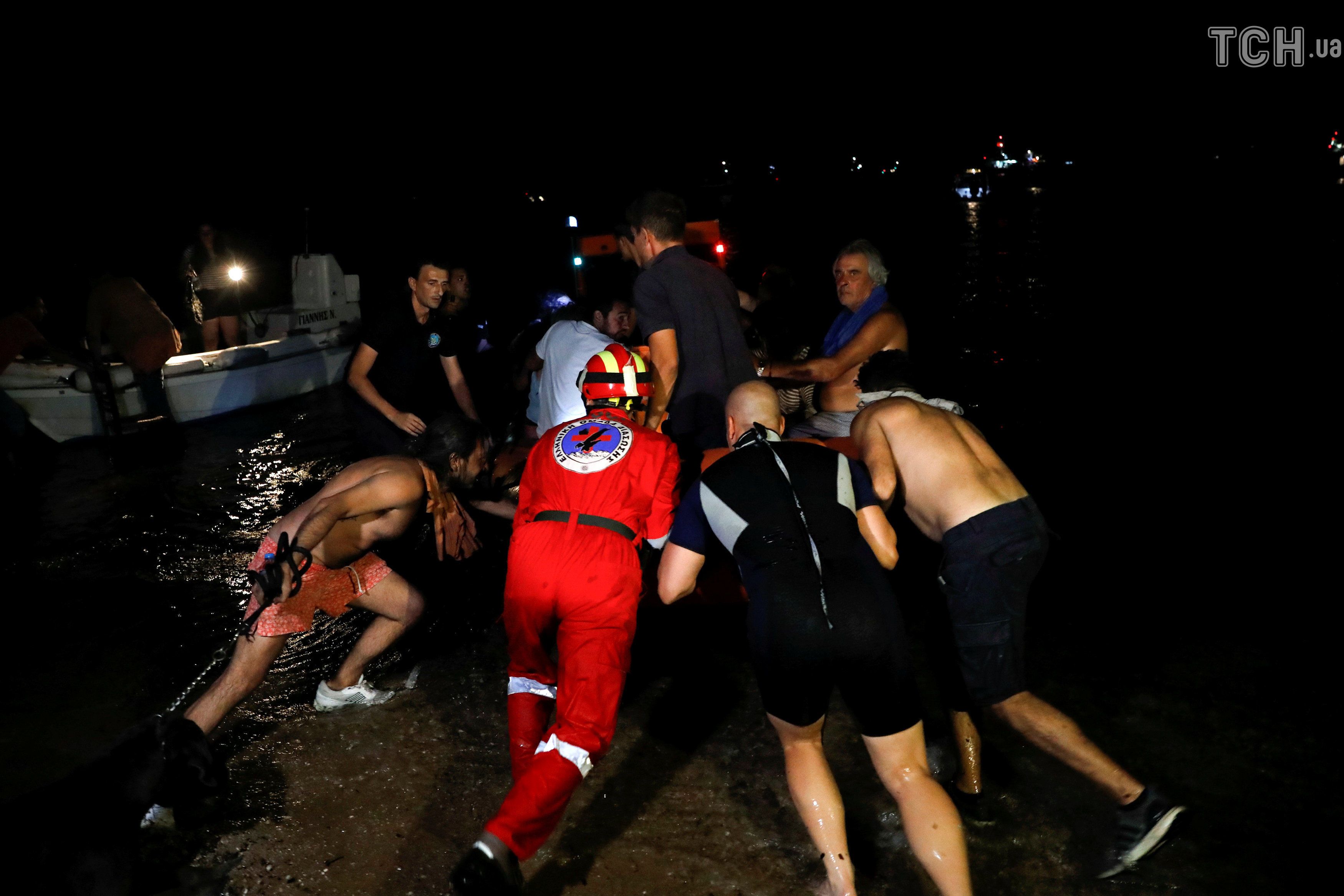 Рятувальники і волонтери підштовхують надувний човен. Місцеві жителі евакуюються під час пожежі в селі Маті. / © Reuters