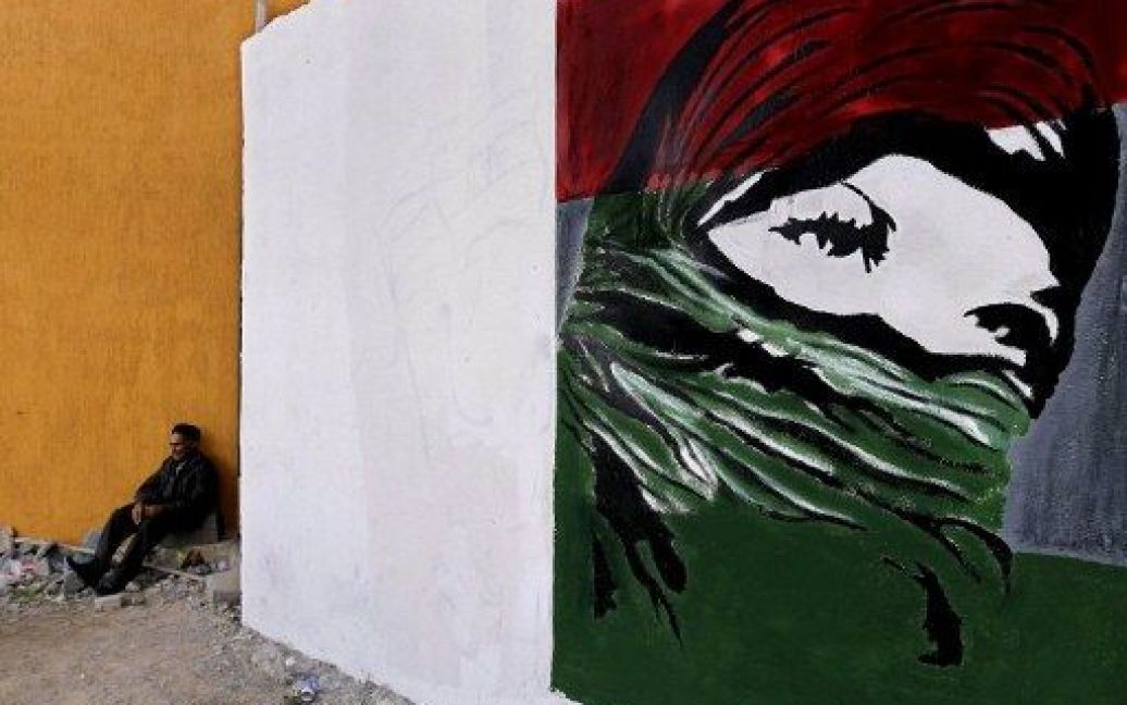 Лівійська Арабська Джамахірія, Тріполі. Чоловік сидить на розі вулиці поруч з графіті, що зображує жінку, одягнену у революційний прапор. / © AFP