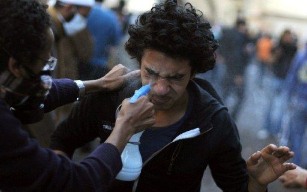 Єгипет, Каїр. Єгипетському демонстранту допомагають вмити обличчя після того, як у нього потрапив сльозогінний газ. Поліція та сили безпеки розганяють демонстрантів на площі Тахрір у Каїрі. Між поліцією та демонстрантами спалахують жорсткі сутички. / © AFP