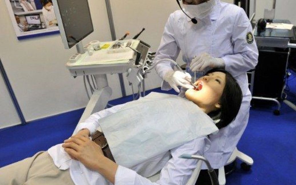 Японія, Токіо. Співробітник лікарні Nippon тестує робота-гуманоїда "Simroid" на Міжнародній виставці роботів у Токіо. Робот був розроблений японською компанією Kokoro для лікарів-стоматологів та студентів. "Сімроїд" має датчики в роті, які викликають звук "Ой", коли стоматолог неправильно лікує "пацієнта". / © AFP