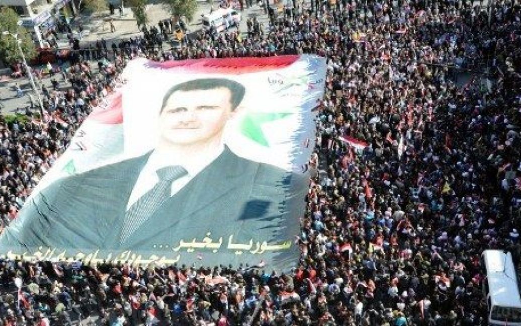 Сирія, Дамаск. Сирійці тримають національний прапор і величезний портрет президента Сирії Башара аль-Асада під час мітингу на його підтримку в центрі Дамаску. / © AFP