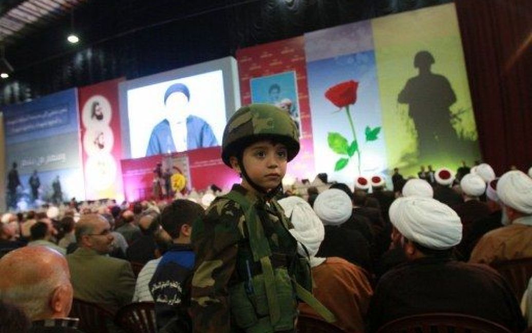 Ліван, Бейрут. Хлопчик у військовій формі руху "Хезболла" разом з шиїтськими мусульманськими священнослужителями слухає виступ лідера бойової групи Хасана Насраллу за допомогою відеозв&#039;язку. / © AFP