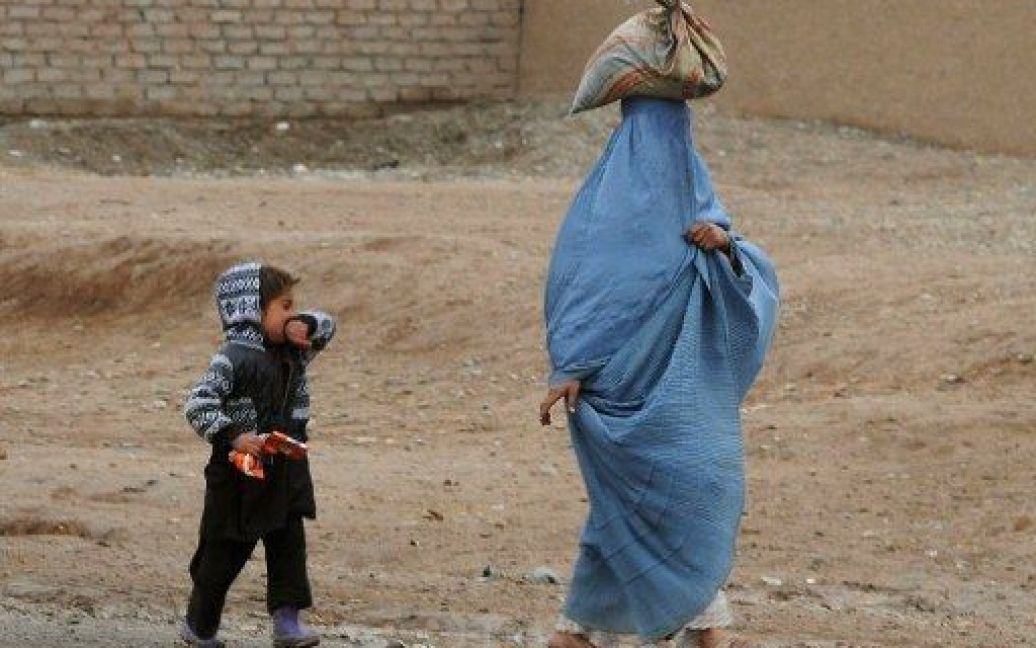 Афганістан, Герат. Жінка несе на голові пакунок під час прогулянки зі своєю дитиною. Міжнародне співтовариство пообіцяло забезпечити довгострокову фінансову підтримку Афганістану після того, як сили НАТО залишать країну у 2014 році. / © AFP