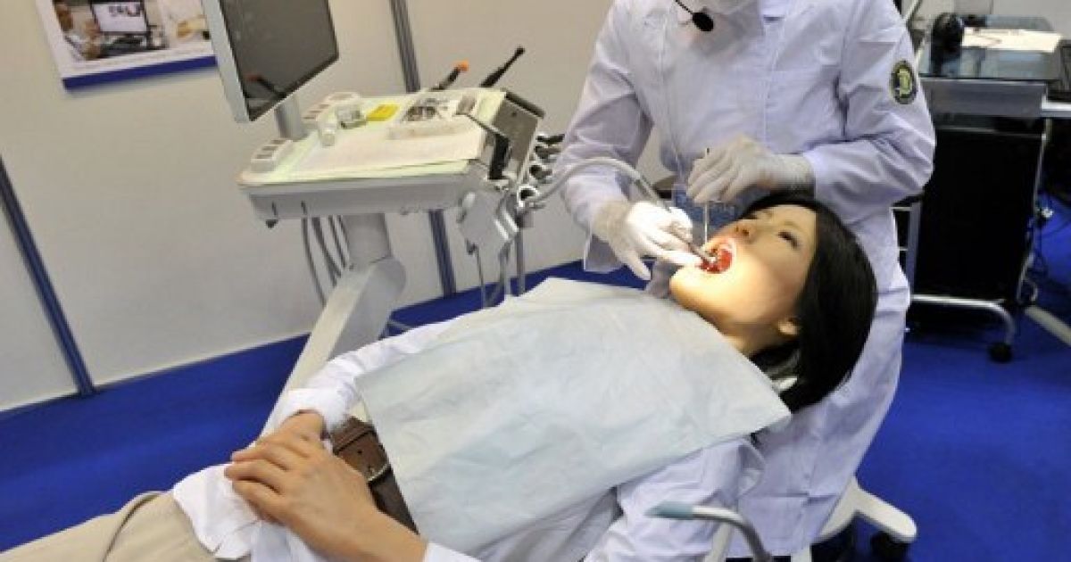Японія, Токіо. Співробітник лікарні Nippon тестує робота-гуманоїда "Simroid" на Міжнародній виставці роботів у Токіо. Робот був розроблений японською компанією Kokoro для лікарів-стоматологів та студентів. "Сімроїд" має датчики в роті, які викликають звук "Ой", коли стоматолог неправильно лікує "пацієнта". / © AFP