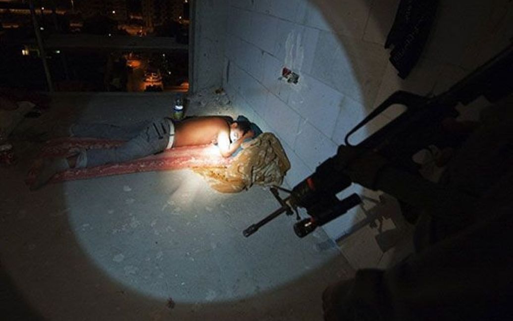 Ізраїль, Ашкелон. Ізраїльський поліцейський прикордонник світить ліхтариком на нелегального палестинського працівника з Західного берега, доки той спить за межами будівельного майданчика у ізраїльському місті Ашкелон. На світанку поліція провела у Ашкелоні спеціальну операцію із пошуку і затримки нелегальних палестинських робітників у Ізраїлі. / © AFP