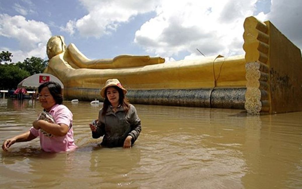 Туристи йдуть по затопленій площі поблизу величезної статуї Будди у тайському місті Аюттхая. Внаслідок раптових повеней у Таїланді загинули 7 людей. / © AFP