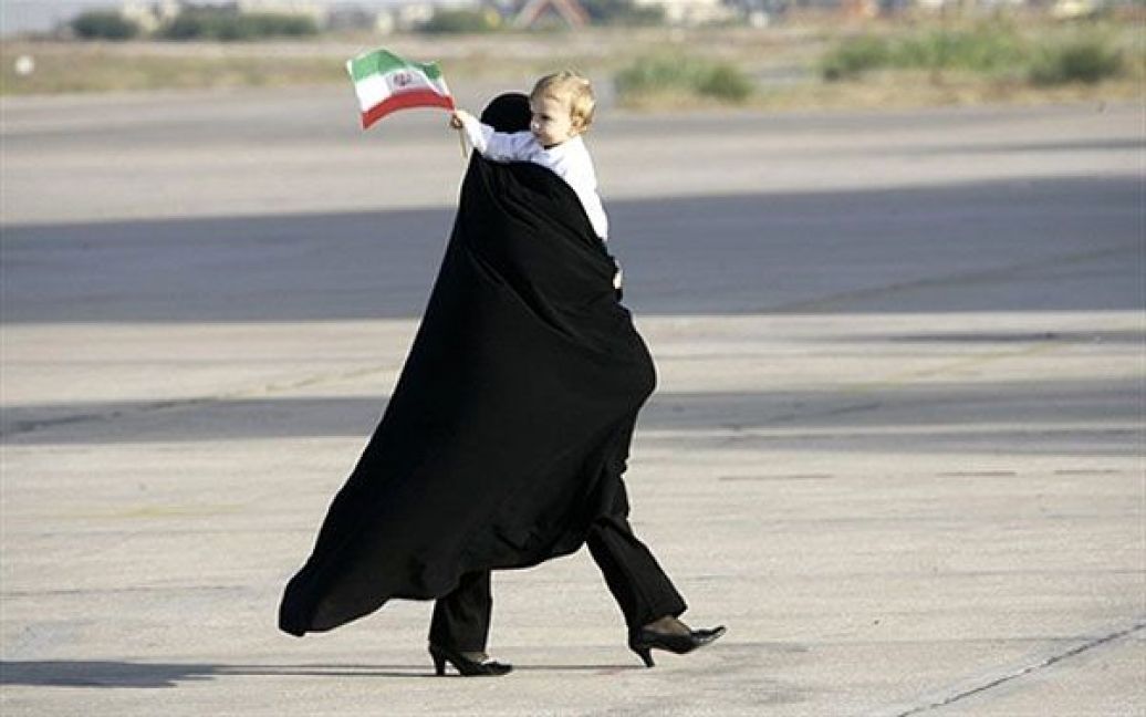 Ліван, Бейрут. Іранська жінка несе на руках дитину, що тримає в руці прапорець, доки вона чекає на прибуття до міжнародного аеропорту Бейрута президента Ірану Махмуда Ахмадінежада. Махмуд Ахмадінежад здійснює свій перший візит на схід Лівану. Кульмінацією дводенного візиту Ахмадінежада має стати відвідання лівано-ізраїльського кордону. / © AFP