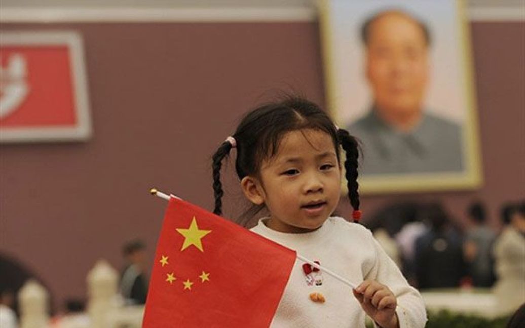 Пекін, Китай. Молода дівчинка тримає китайський прапор перед воротами Тяньаньмень у Пекіні під час святкувань Національного дня Китаю. Тисячі китайців зібралися на площі, щоб відзначити 61-у річницю з дня заснування Китайської Народної Республіки. / © AFP