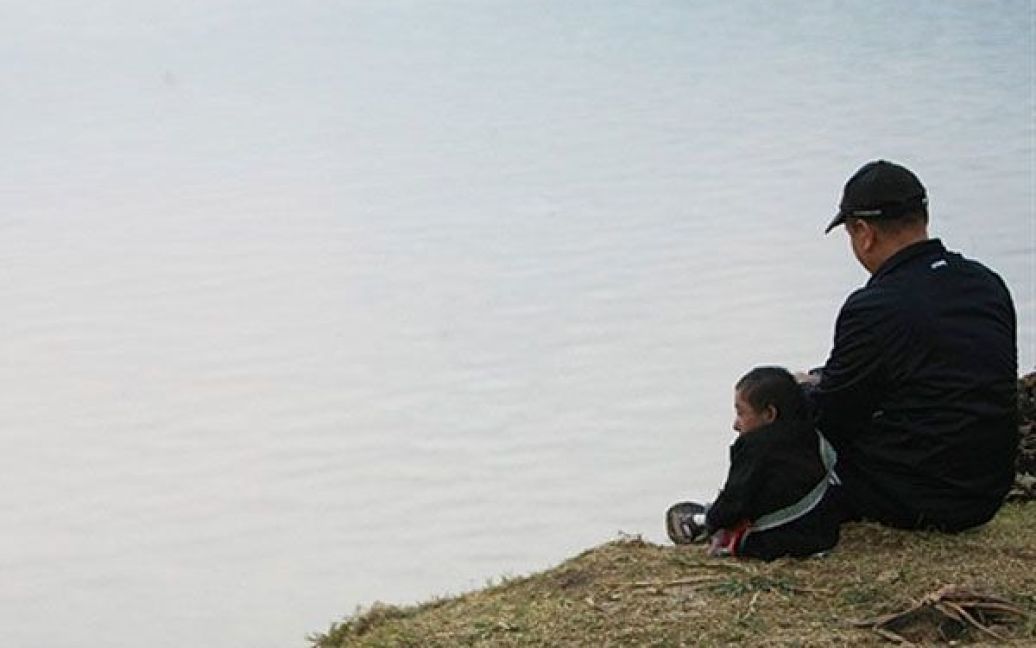 Магар і його батько сидять на березі озера. / © AFP