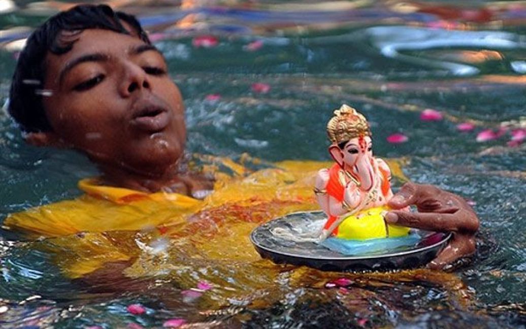 Індія, Мумбаї. Індійський хлопчик плаває з фігуркою індуїстського бога Ганеші у штучному екологічному ставку у Мумбаї. Індуїсти вірять, що Ганеша може допомогти усунути перешкоди, принести благословення мудрості і процвітання. Глиняні та гіпсові фігурки богів занурюють у воду на перший, третій, п&#039;ятий і останній дні свята Ганеші, яке щорічно відзначається по всій Індії. / © AFP