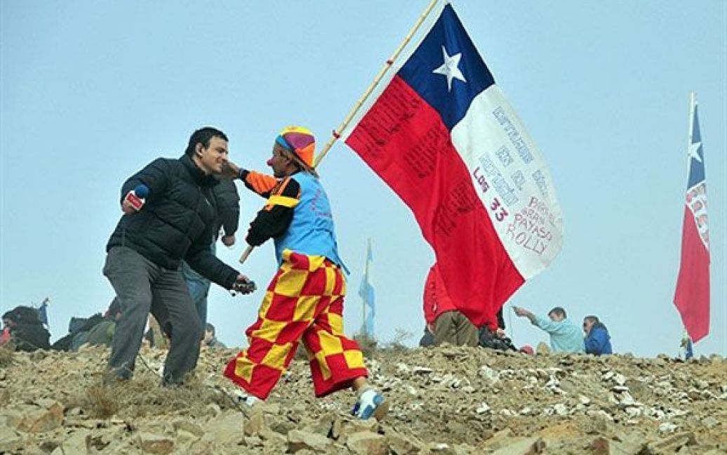 Чилі, Копіапо. Чоловік у костюмі клоуна з чилійським прапором вітає тележурналіста після вдалих робіт з порятунку 33 гірників, які перебувають у пастці під землею. Після двох місяців, проведених під землею, шахтарі всього за кілька днів можуть бути врятовані. / © AFP