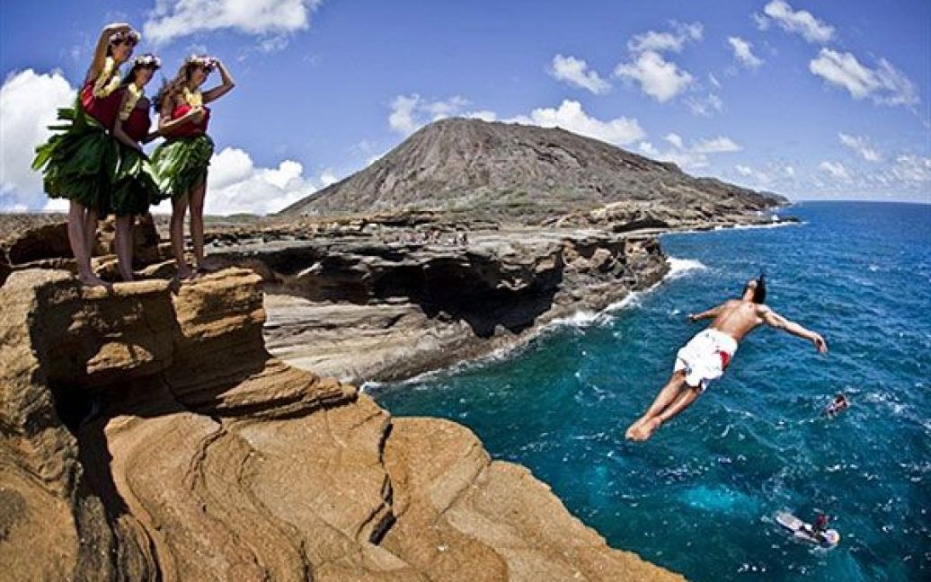 США, Оаху. Колумбієць Орландо Дуке стрибає з 16-метрової скелі у Лана&rsquo;і Лукаут (Lana&#039;i Lookout), доки місцеві дівчата дивляться на його стрибок. На Гавайях готуються до фіналу світових змагань з кліфф-дайвінгу 2010 Red Bull Cliff Diving World Series. / © AFP