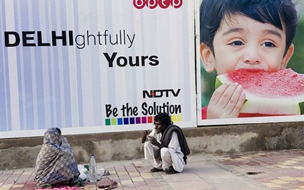 Індія, Нью-Делі. Безпритульна пара обідає на землі перед рекламним плакатом у Нью-Делі. В індійській столиці з 3 по 14 жовтня мають відбутися Ігри Співдружності, найбільша спортивна подія у місті з 1982 року. / © AFP
