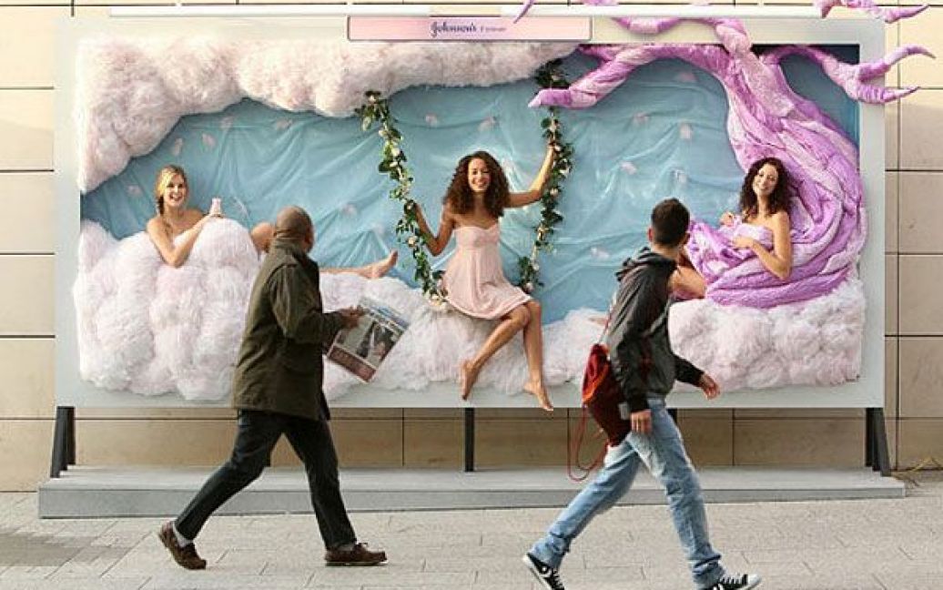 Великобританія, Лондон. Люди проходять повз рекламний плакат з живими моделями, які рекламують лосьон для тіла у торговому центрі Westfield. / © The Telegraph