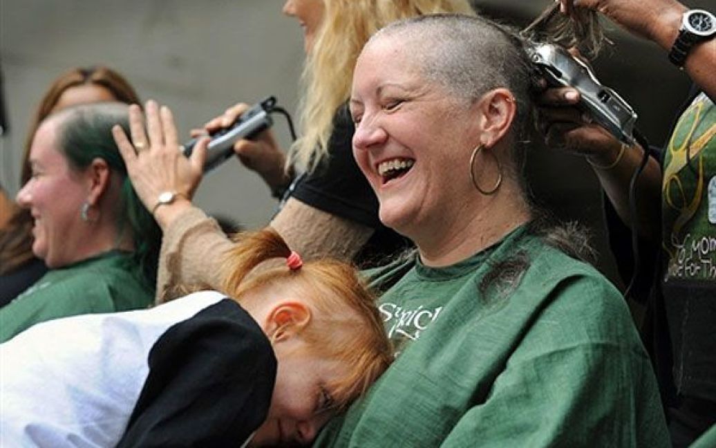 США, Голлівуд. Ребека Хам дивиться на свою 8-річну дочку Грейс Кері, яка з дитинства хворіє на рак. 46 матерів провели акцію підтримки, щоб зібрати гроші для досліджень, спрямованих на пошук ліків від раку. Жінки обрили собі голови на підтримку Фонду Санкт-Болдріку у Голлівуді, який проводить подібні акції. Цього разу жінки намагаються зібрати щонайменше 1 мільйон доларів на дослідження ліків від дитячих онкологічних захворювань. / © AFP