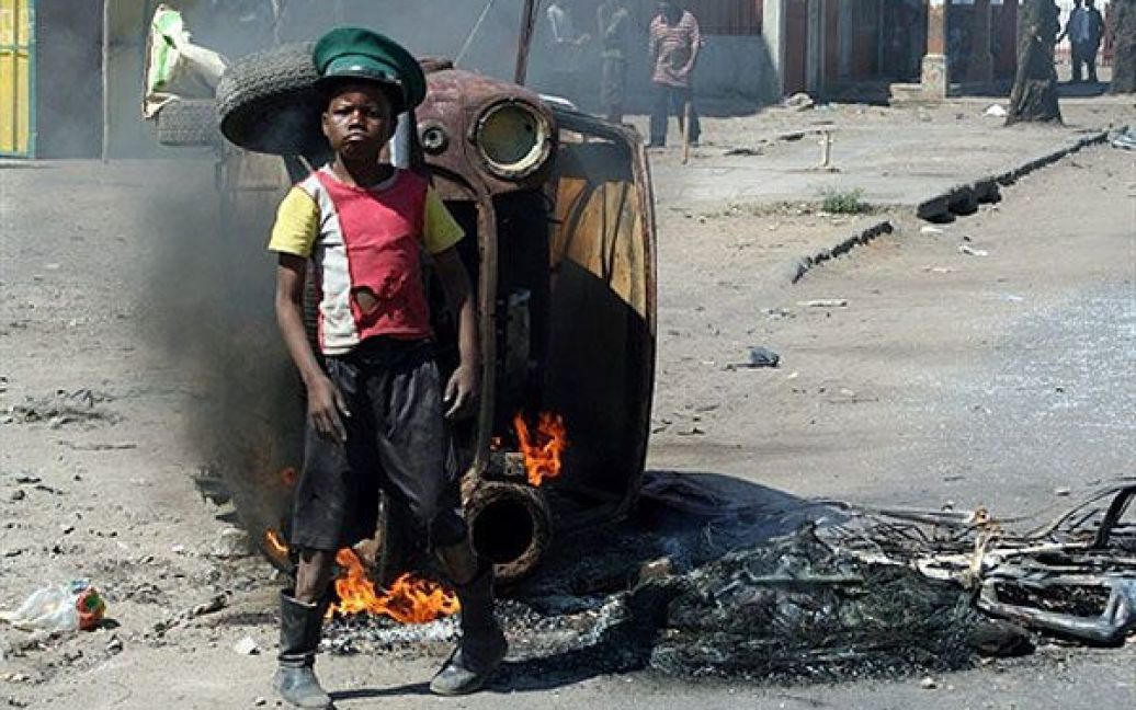 Мозамбік, Мапуту. Мозамбікський хлопчик-демонстрант стоїть поруч із палаючим автомобем на одній з вулиць міста Мапуту. Мозамбіцька поліція посилила патрулювання вулиць столиці, а президент країни Армандо Гебуза закликав до спокою після того, як у місті спалахнули продовольчий бунт і протести проти зростання цін на паливо. В результаті заворушень чотири людини загинули. Поліція розчищала вулиці від барикад і палаючих коліс. Президент Гебуза заявив, що він розуміє гнів людей з приводу зростання цін, але його засмутили насильницькі методи: "Сумно, що люди використали право на мирні демонстрації, аби перетворити їх на насильницькі протести". / © AFP