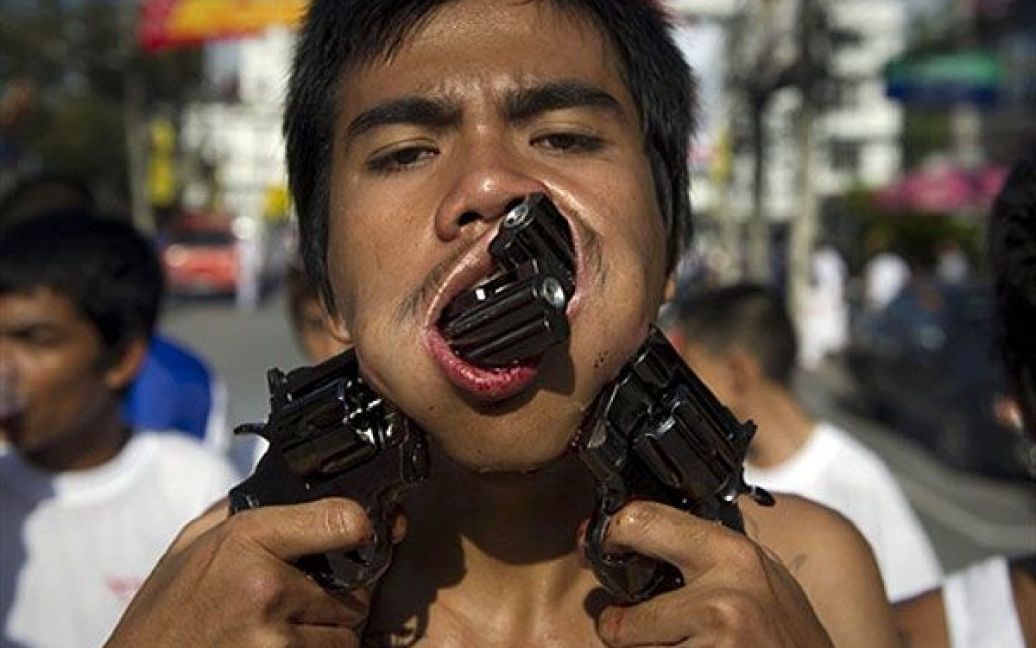 Таїланд, Пхукет. Віруючий проткнув свої щоки іграшковими пістолетами під час участі у процесії на честь щорічного вегетаріанського фестивалю у Пхукеті. / © AFP