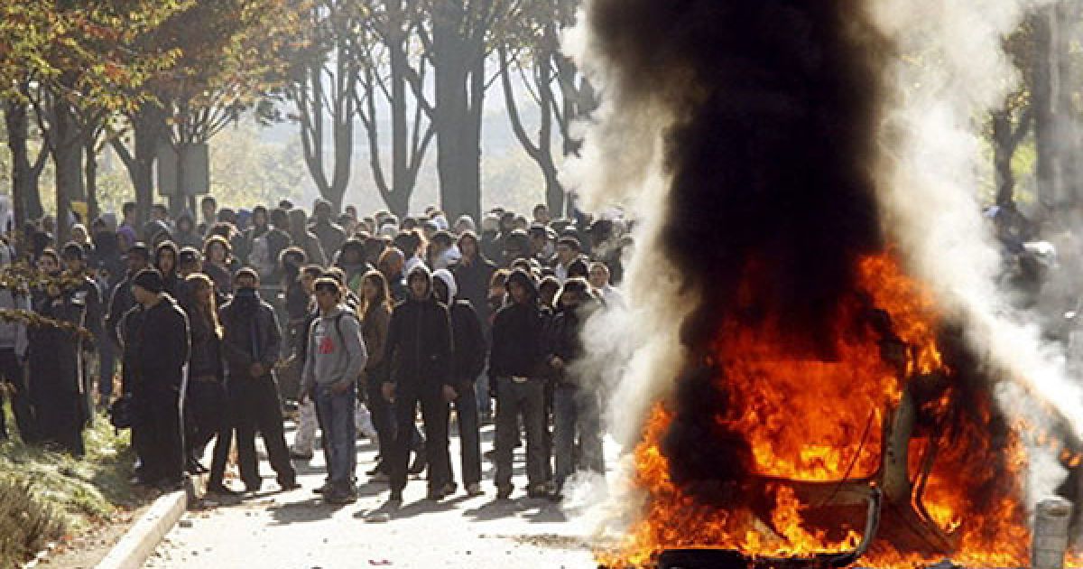 Франція, Нантер. Молодь стоїть поруч із палаючою машиною під час зіткнень з поліцією у передмісті Парижа Нантері. У Франції тривають акції протесту проти урядової пенсійної реформи, в яких беруть участь всі прошарки населення. Уряд створив антикризовий штаб, членам якого доручено зробити все можливе для недопущення в країні повномасштабної паливної кризи, оскільки через страйк було заблоковано сховища бензину. / © AFP