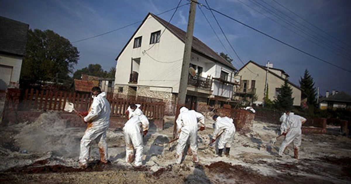 Угорщина, Девечер. Працівники у захисних масках і одязі розкидають гіпс на токсичний червоний шлам, розлитий на вулиці міста Девечер. Угорська влада заявила, що загроза другого виливу токсичних відходів була відвернена, і мешканці зможуть повернутися додому. Завод, який несе відповідальність за аварію, готовий відновити виробництво. / © AFP