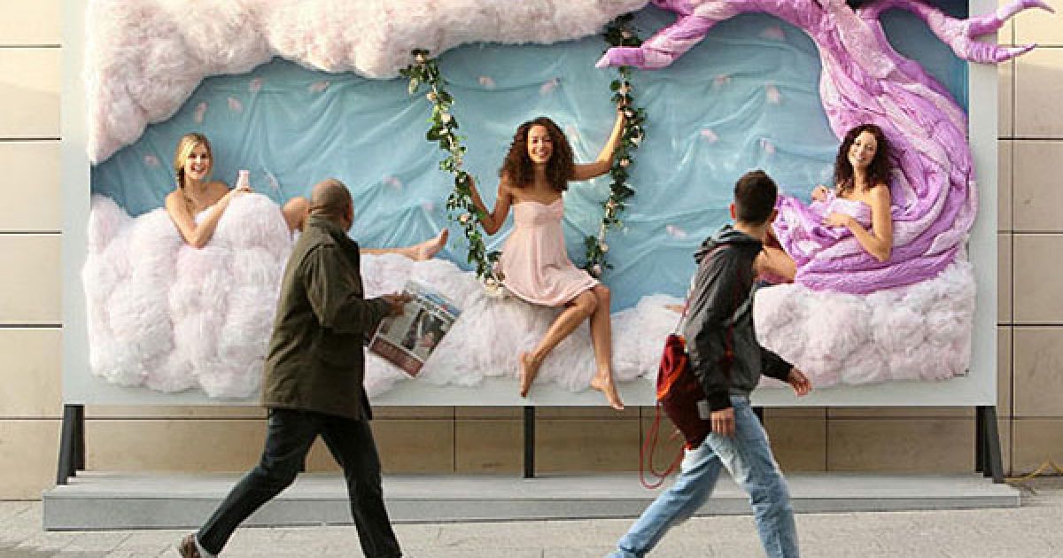 Великобританія, Лондон. Люди проходять повз рекламний плакат з живими моделями, які рекламують лосьон для тіла у торговому центрі Westfield. / © The Telegraph