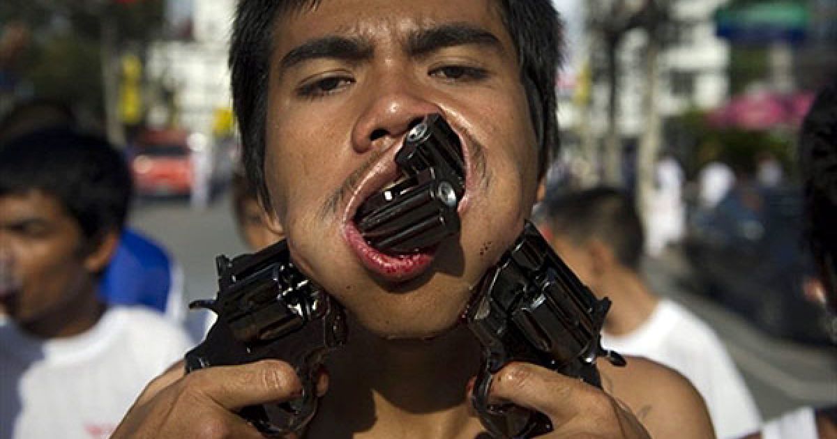 Таїланд, Пхукет. Віруючий проткнув свої щоки іграшковими пістолетами під час участі у процесії на честь щорічного вегетаріанського фестивалю у Пхукеті. / © AFP