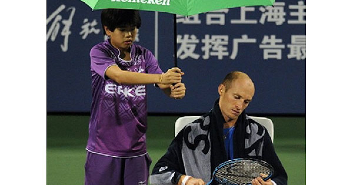 Китай, Шанхай. Російський тенісист Микола Давиденко перевіряє свою ракетку, доки хлопчик-асистент тримає над ним парасольку від дощу, перед матчем проти Міши Звєрєва з Німеччини. Звєрєв виграв перший сет 6-4, а Давиденко вів у другому 3-2, коли відкритий матч був зупинений через дощ. / © AFP