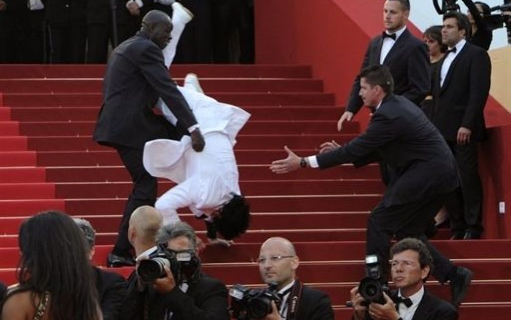 Франція, Канни. Охоронець намагається втримати гостя, який впав під час спроби виконати трюк на червоній доріжці перед церемонією на честь французького актора Жан-Поля Бельмондо на 64-ому Каннському кінофестивалі. / © AFP