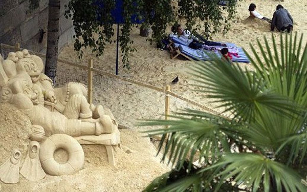 Франція, Париж. Жінка лежить на шезлонгу біля піщаної скульптури "Мінні і Міккі Маус" на набережній Сени в Парижі під час відкриття щорічного "Паризького пляжу". Десятий рік поспіль береги Сени перетворюють на повноцінні пляжі з пальмами, душами і гамаками. / © AFP