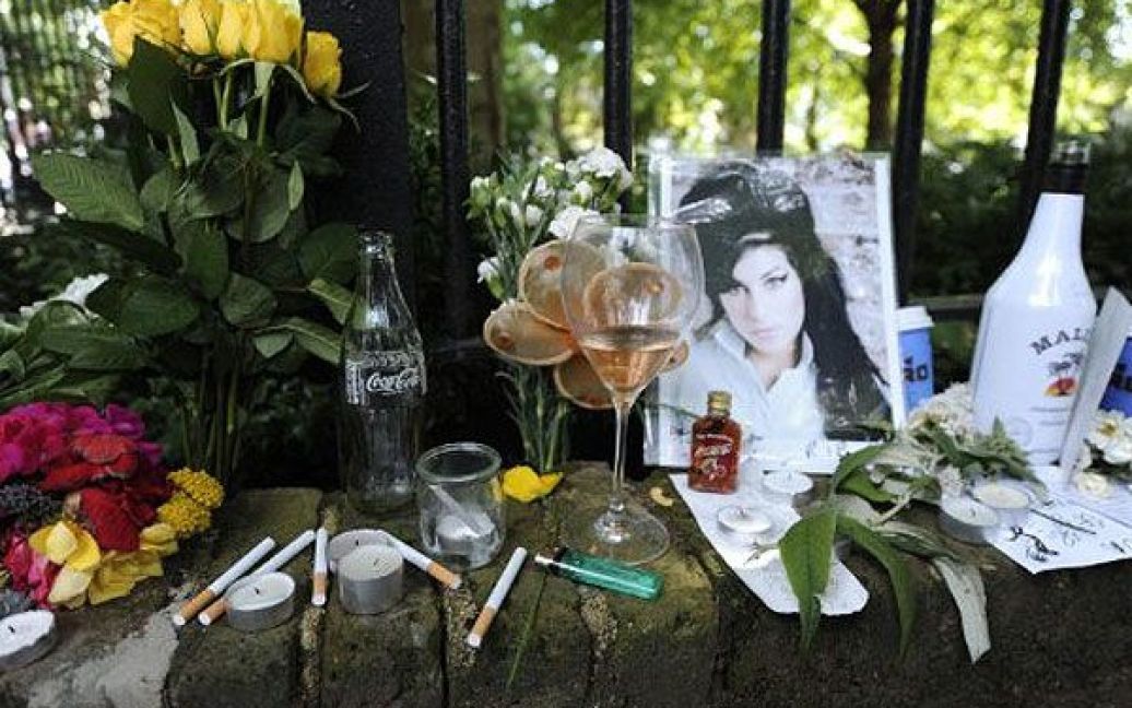 Великобританія, Лондон. Сигарети, алкоголь і фотографія з квітами стоять поблизу будинку британської співачки, поп-зірки Емі Уайнхаус, яку знайшли в її квартирі мертвою. Емі Уайнхаус було 27 років. / © AFP