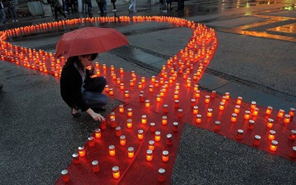 Сербія, Белград. Жінка запалює свічку і встановлює її на символічну червону стрічку, яку виклали в Белграді на згадку про тих, хто вмер від СНІДу, під час відзначення Всесвітнього дня пам&rsquo;яті людей, які померли від СНІДу. / © AFP