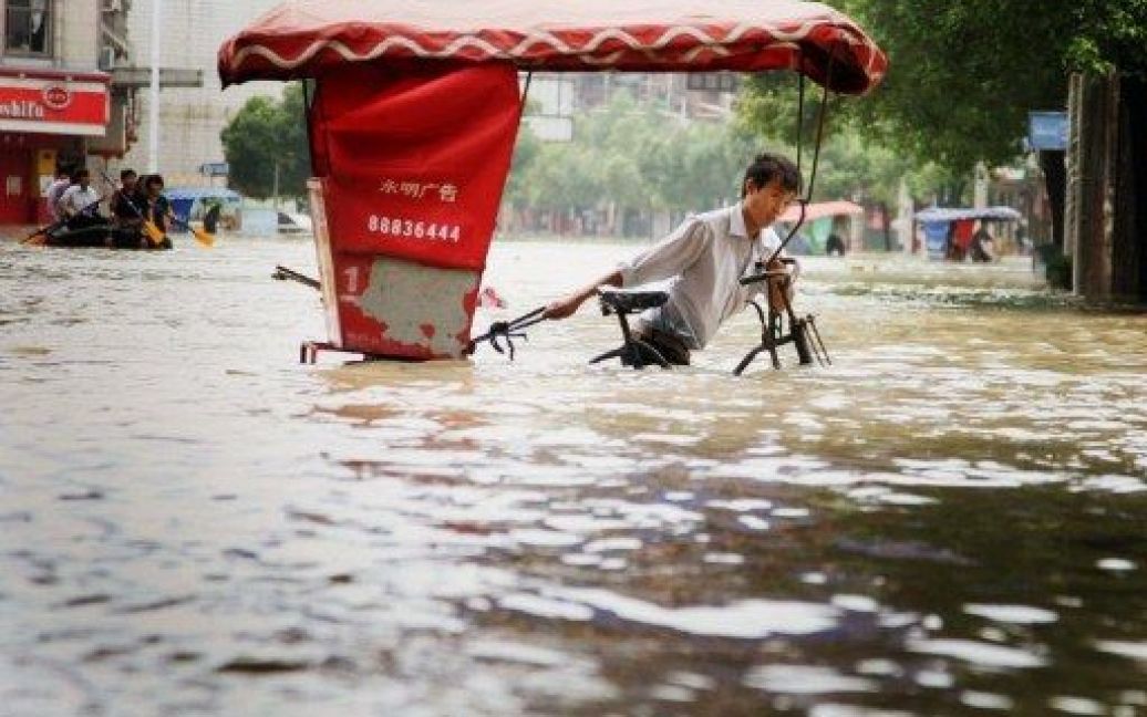 Китай, Ланкі. Чоловік їде на велосипеді через затоплену вулицю у східній провінції Китаю. Постраждалі від повені райони центрального та південного Китаю готуються до нового удару стихії. / © AFP