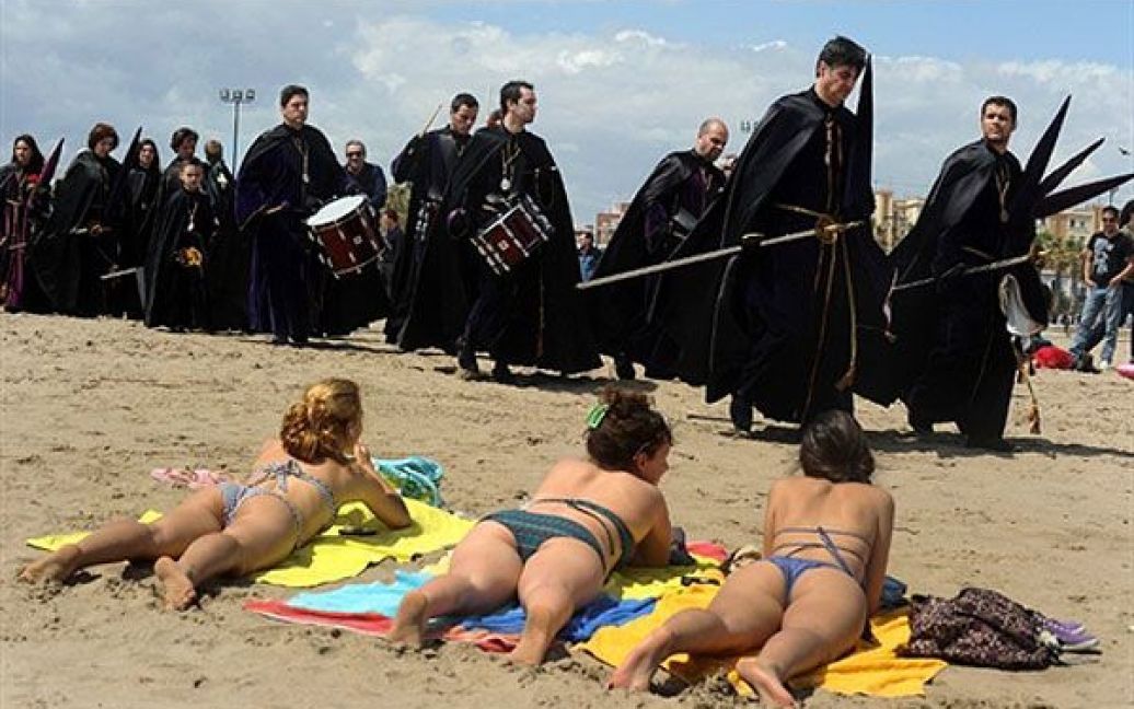 Іспанія, Валенсія. Члени релігійного братства "Cristo Salvador y del Amparo" беруть участь у ході перед жінками, які засмагають на пляжі Валенсії. / © AFP