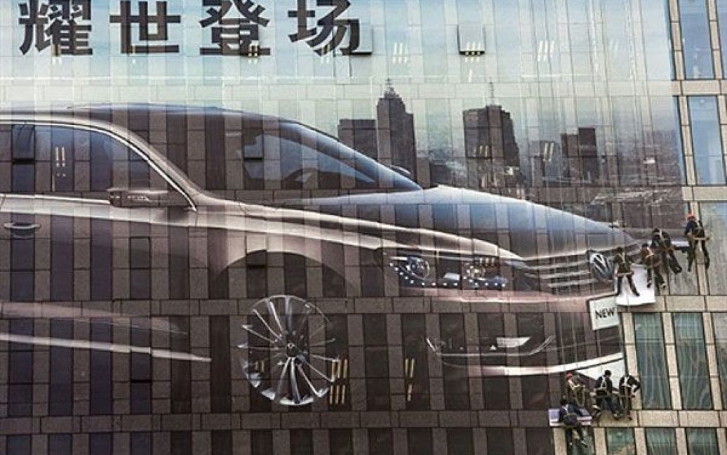 Китай, Шанхай. Китайські працівники встановлюють гігантську рекламу автомобіля на висотну будівлю поруч з місцем проведення Шанхайського автошоу, яке починається 21 квітня і триватиме до 28 квітня. / © AFP