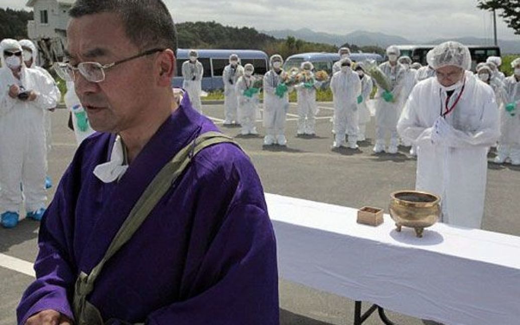 Японія, Окума. Буддійський монах співає сутри, доки колишні жителі міста Окума моляться поблизу аварійної АЕС "Фукусіма" про жертв землетрусу та цунамі 11 березня. На поминальній службі були присутні близько 40 осіб у костюмах радіаційного захисту. / © AFP
