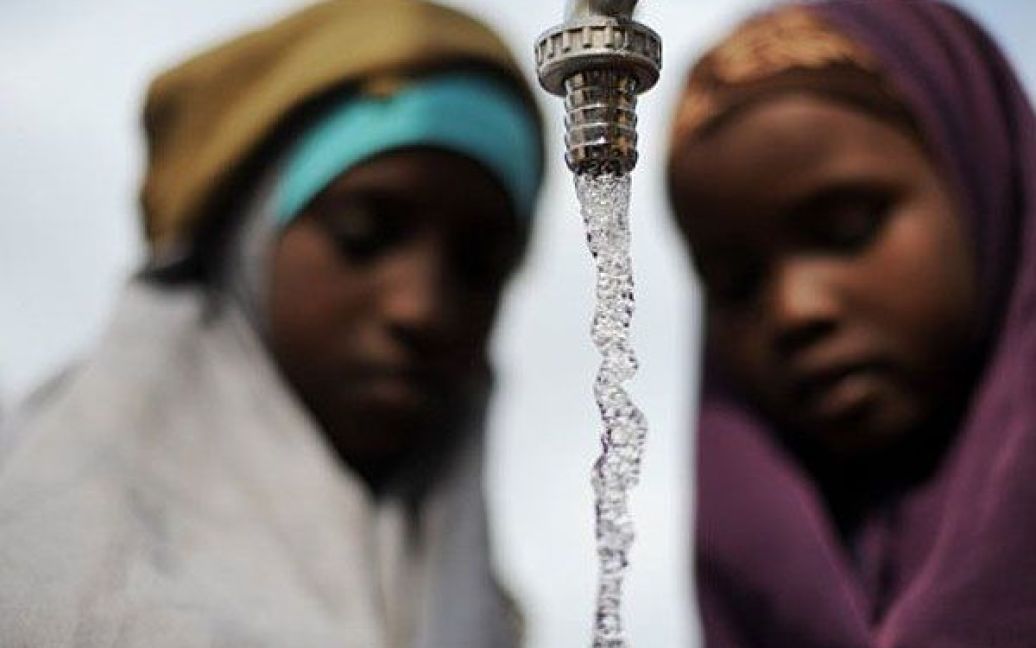 Кенія, Дадааб. Сомалійські дівчатка дивляться на воду, доки вони заповнюють каністри. У найбільшому в світі таборі біженців в Дадаабі виникли серйозні проблеми з водою. До 370 тисяч мешканців додались тисячі сомалійців, які потерпають від посухи. / © AFP