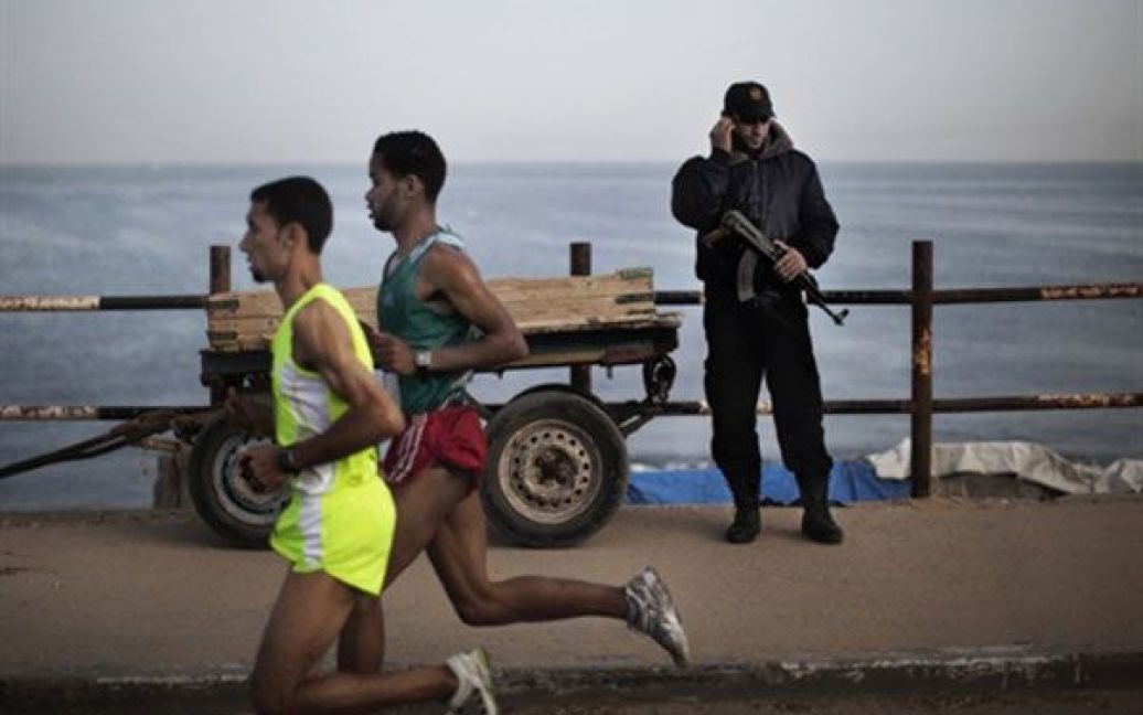 Місто Газа. Поліцейський з руху ХАМАС говорить по телефону, доки палестинський спортсмен, олімпієць Надер Масрі пробігає повз нього під час першого в історії марафону, що провели у секторі Газа. / © AFP