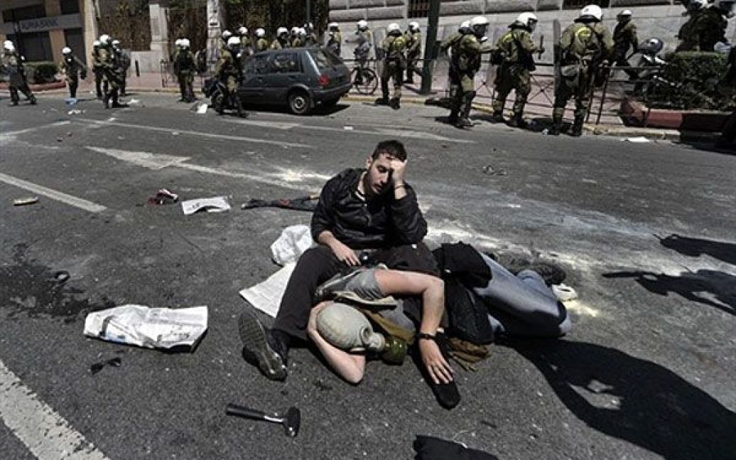 Греція, Афіни. Демонстрант сидить на тротуар поруч із пораненою людиною після зіткнення з грецькою поліцією. Акцію протесту в Афінах, в якій брали участь тисячі людей, жорстоко розігнала поліція. / © AFP