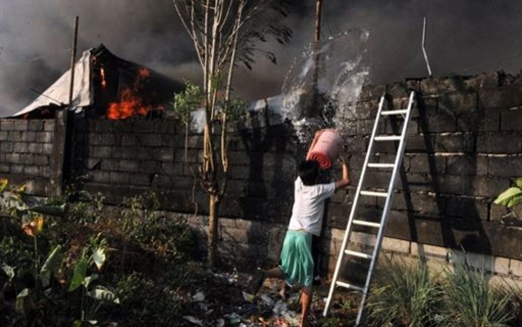 Філіппіни, Маніла. Людина намагається загасити будинок, який загорівся під час пожежі у нетрях в Манілі. В результаті пожежі, близько 200 будинків були зруйновані, більше 600 сімей постраждали. / © AFP