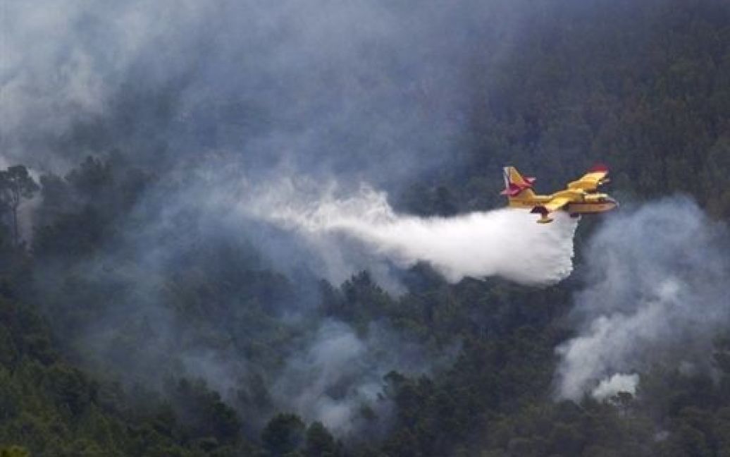 Іспанія, Сан-Хуан де Лабрітья. Пожежний гелікоптер розпилює воду на палаючий лісовий масив у Серра-де-Монар на іспанському острові Ібіца. Поліція Іспанії затримала підозрюваних у випадковому підпалі, який спричинив найбільшу пожежа за всю історію острові Ібіца. / © AFP