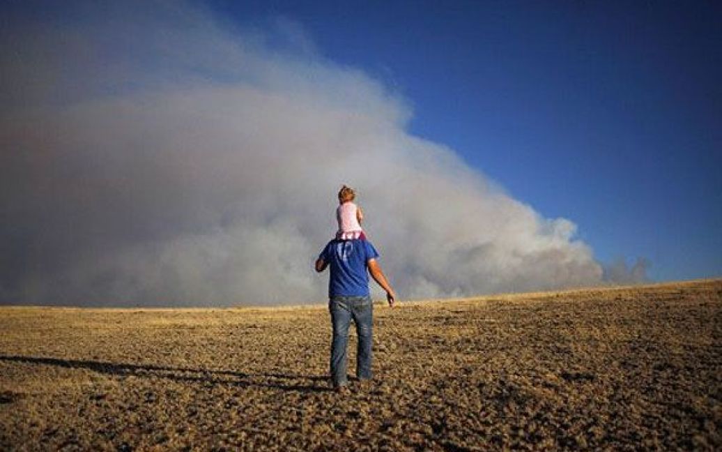 США, Спрінгервіль, штат Арізона. Чоловік з дитиною піднімаються на пагорб, щоб подивитись на лісову пожежу, яка охопила територію навколо міста. Сотні тисяч гектарів продовжують горіти у східній частині штату Арізона. Тисячі місцевих жителів були евакуйовані. / © AFP