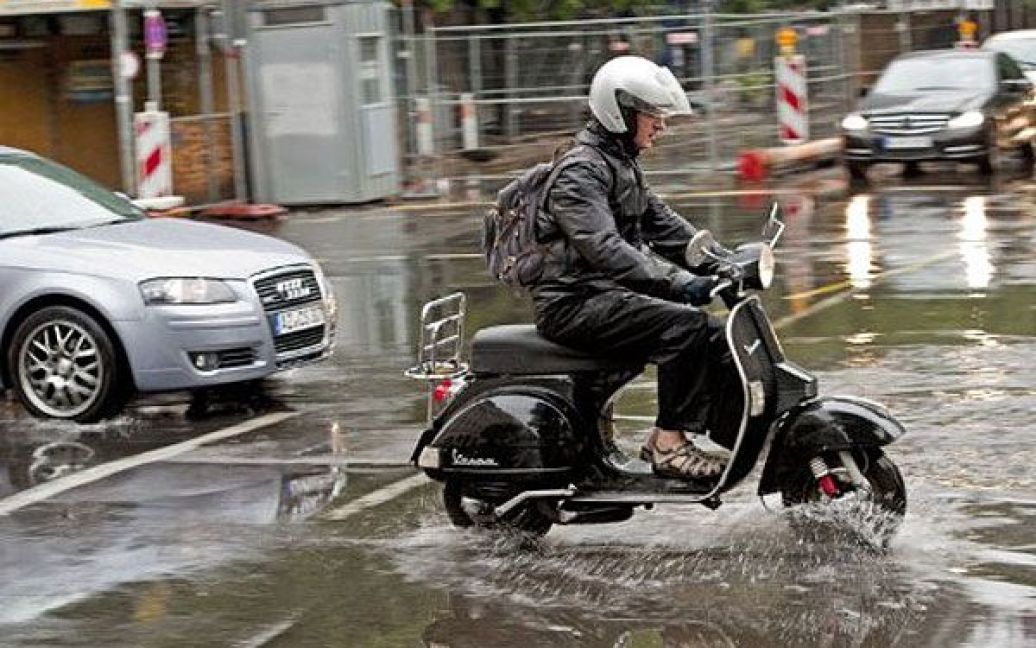 Німеччина, Берлін. Чоловік веде свій велосипед через залиту дощем вулицю в Берліні. Метеорологи прогнозують подальші опади у німецькій столиці. / © AFP
