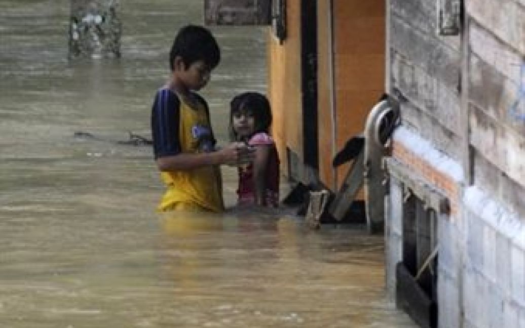 Таїланд, Чанг. Тайські діти стоять на затопленій вулиці після проливних дощів у південній провінції Таїланду Чанг. В результаті сильної повені на півдні Таїланду, загинуло 25 осіб, тисячі були евакуйовані. / © AFP