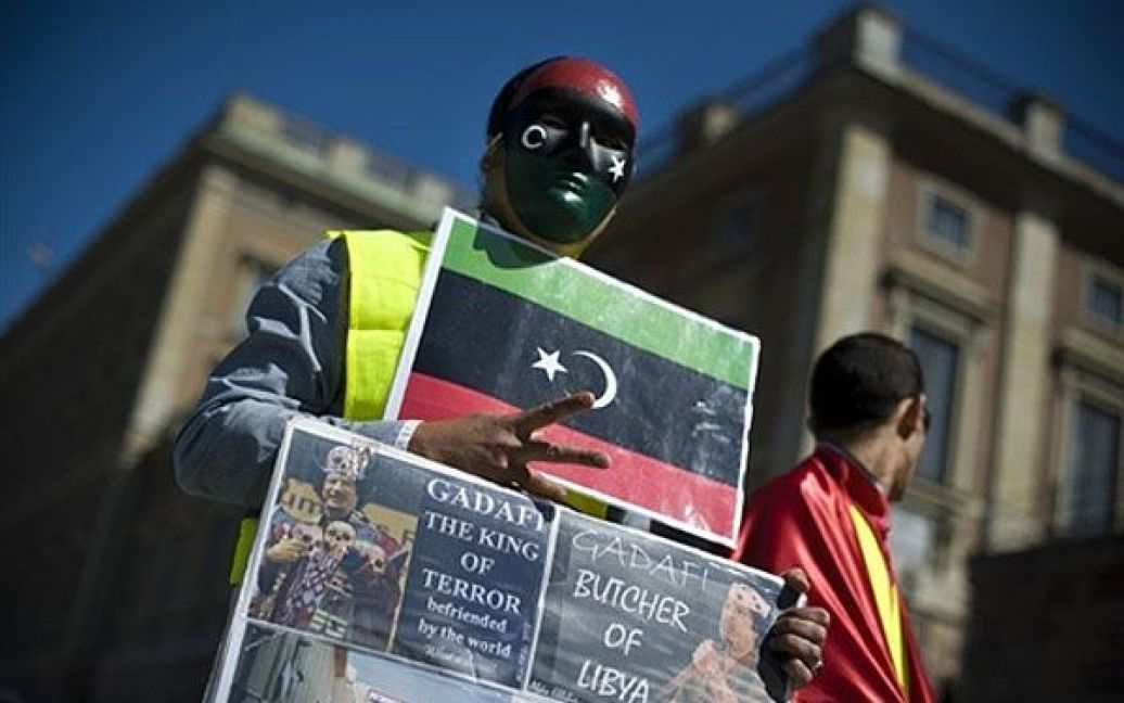 Швеція, Стокгольм. Людина у масці з прапором Лівійської монархії бере участь в акції на підтримку лівійських повстанців у Стокгольмі. НАТО заявила, що військові літаки розгромили вісім кораблів ВМФ Муаммара Каддафі. / © AFP