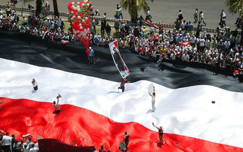 Сирія, Дамаск. Сирійці несуть гігантський національний прапор під час провладної демонстрації у місті Дамаск. / © AFP